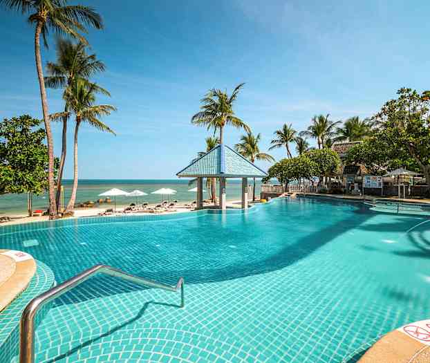 Et utendørs basseng ved en sandstrand med palmer og solsenger. (AI-generert tekst)