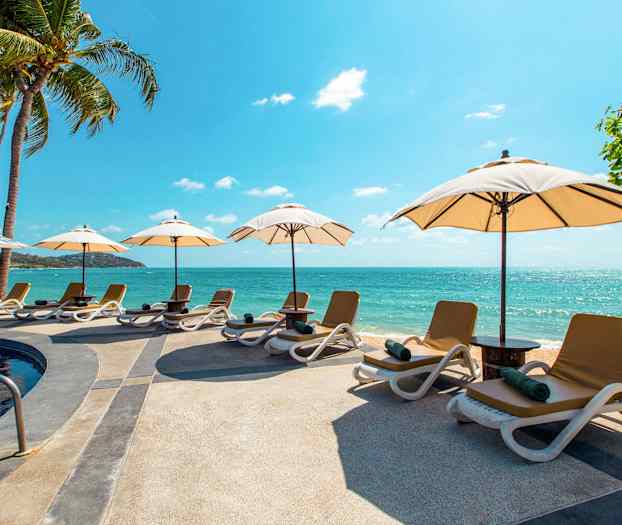 Strand med solsenger og parasoller ved et basseng nær havet. (AI-generert tekst)