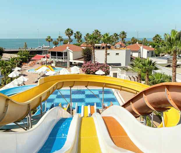 Flere fargerike vannsklier fører ned til et basseng med palmer og bygninger i bakgrunnen. (AI-generert tekst)