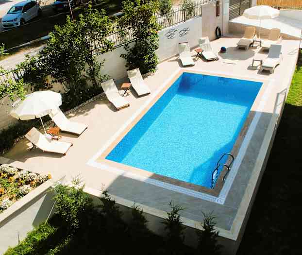 Et rektangulært basseng med solsenger og parasoller ved siden. (AI-generert tekst)