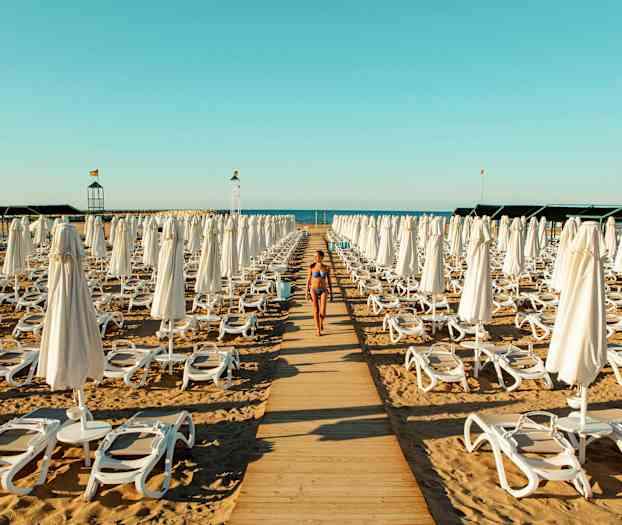 En kvinne i bikini går på en gangvei av tre mellom solsenger og parasoller på en strand. (AI-generert tekst)