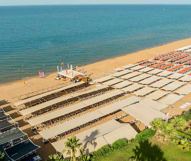 En sandstrand med solskjerming med solsenger under. (AI-generert tekst)