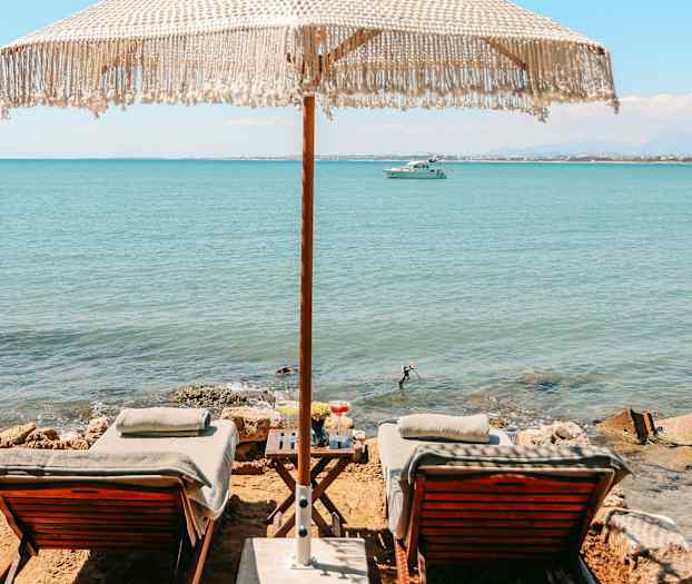 To solsenger med parasoll ved sjøen. (AI-generert tekst)