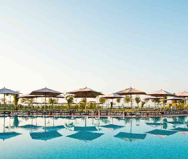 Et svømmebasseng med solsenger og parasoller langs kanten. (AI-generert tekst)