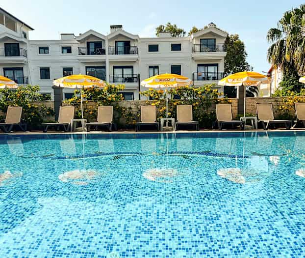 Et basseng med solsenger og gule parasoller foran en bygård. (AI-generert tekst)