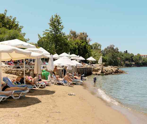 Badestrand med solsenger og parasoller ved en vannkant med klart vann. (AI-generert tekst)