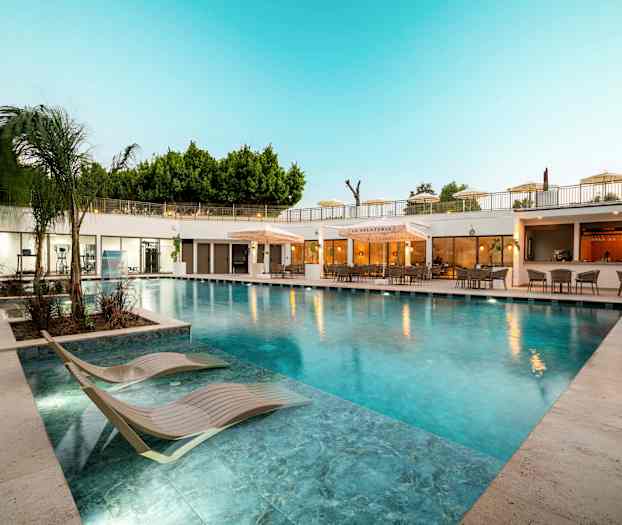 Utendørsbasseng med solsenger og restaurant i bakgrunnen. (AI-generert tekst)