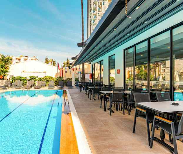 Et basseng på et hotell med solsenger og en tilstøtende spiseplass. (AI-generert tekst)