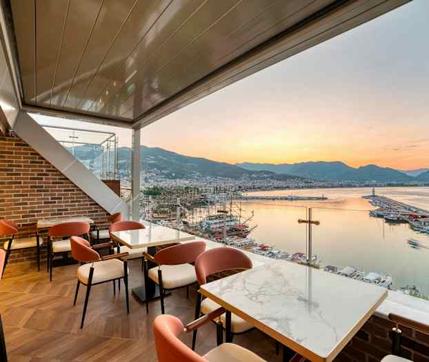 Restaurant med utsikt over en havn, sjøen og fjellene ved solnedgang. (AI-generert tekst)