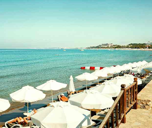 Hvit sandstrand med solsenger og parasoller ved klart blått hav. (AI-generert tekst)