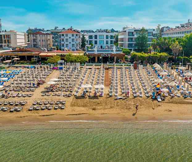 Strand med solsenger og parasoller, omgitt av hoteller og bygninger. (AI-generert tekst)