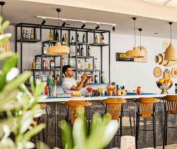 En bar med hyller fylt med flasker og tre trestoler foran. (AI-generert tekst)