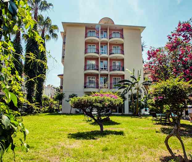 Et leilighetsbygg med balkonger omgitt av grøntområder og blomstrende trær i forgrunnen. (AI-generert tekst)