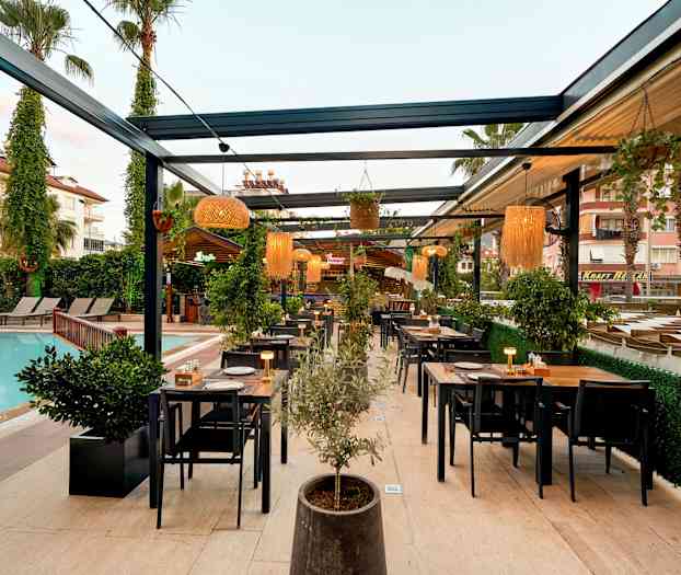 Utendørsrestaurant ved et basseng med bord og stoler samt planter og belysning. (AI-generert tekst)