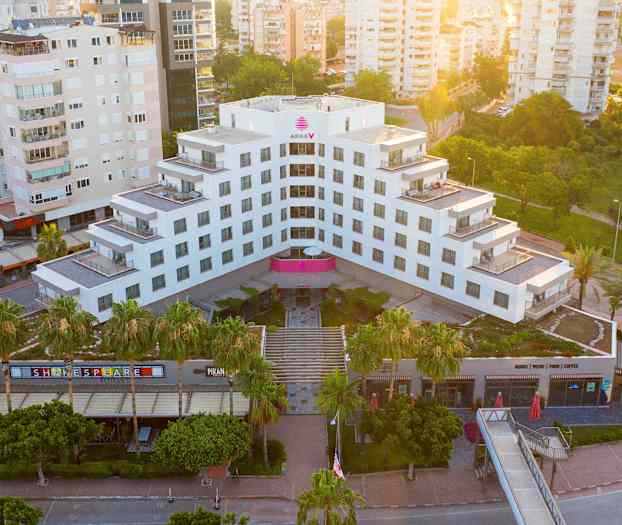 Et moderne hotell omgitt av grøntområder og andre bygninger, sett ovenfra. (AI-generert tekst)