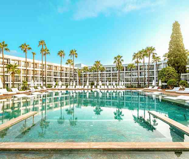 Hotellbasseng med solsenger og parasoller omgitt av palmer og moderne bygninger. (AI-generert tekst)