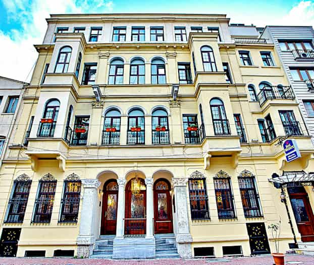 Fasaden av en eldre bygning med balkonger og dekorerte vinduer. (AI-generert tekst)