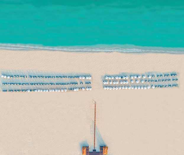 Luftfoto av en strand med solsenger og parasoller ved sjøen. (AI-generert tekst)