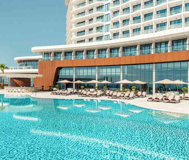 Et hotellkompleks med et stort basseng foran, omgitt av solsenger og parasoller. (AI-generert tekst)