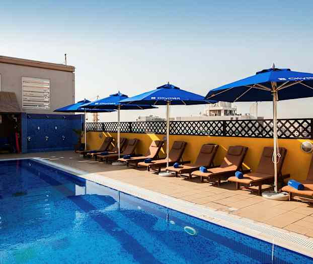 Et svømmebasseng med solsenger og parasoller på siden under en klar himmel. (AI-generert tekst)