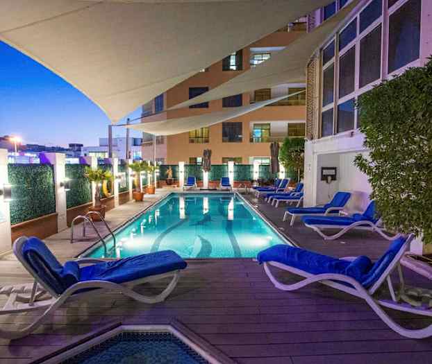 Et opplyst svømmebasseng med omkring liggende solsenger og planter, under et beskyttende seil om kvelden. (AI-generert tekst)