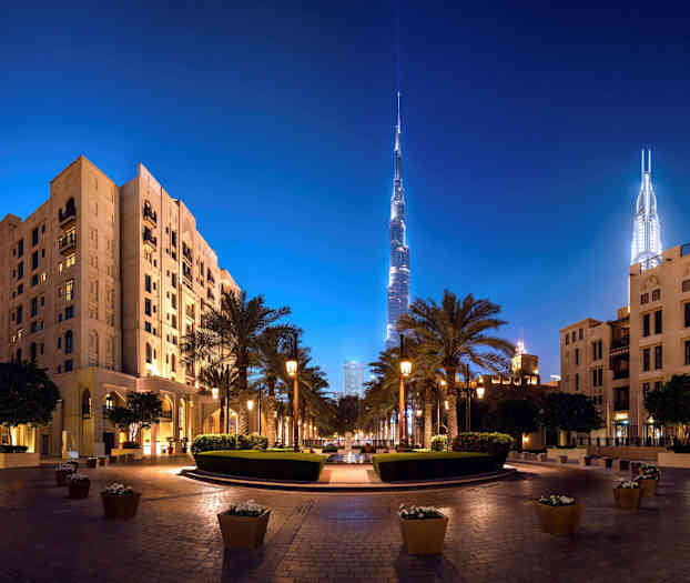 Nattbilde av et bymiljø med høye bygninger og palmer. (AI-generert tekst)