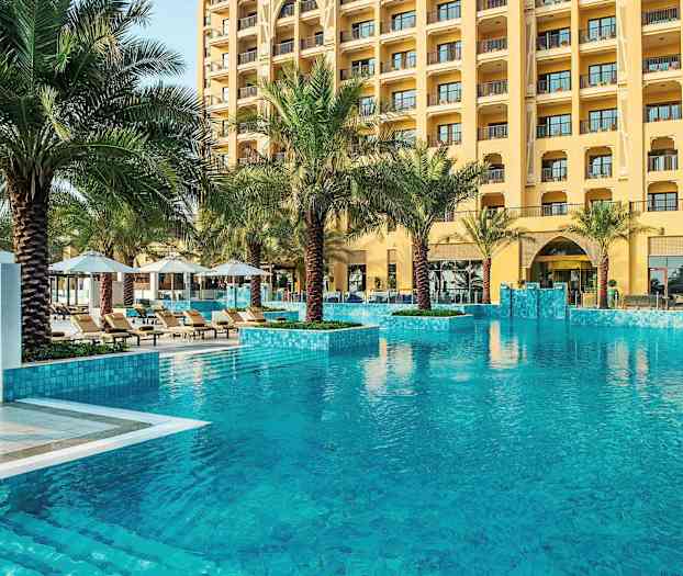 Hotellbasseng med klart vann, omgitt av palmer og solsenger. (AI-generert tekst)