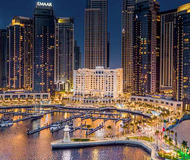 En bysiluett om kvelden med opplyste høye bygninger og en marina i forgrunnen. (AI-generert tekst)