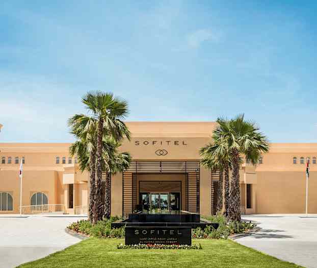 Forsiden av Sofitel-hotell med palmer og flagg. (AI-generert tekst)