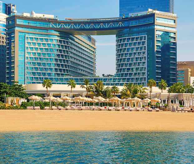 Moderne bygninger ved en strand med parasoller og solsenger. (AI-generert tekst)