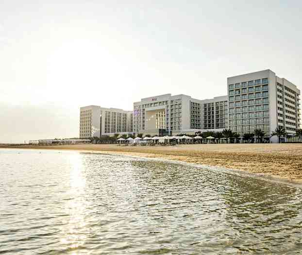 Et stort hotellkompleks ved en strand med hav i forgrunnen. (AI-generert tekst)