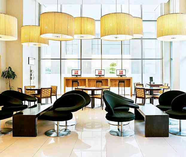 En moderne møblert hotellobby med svarte stoler, bord og datamaskinstasjoner. (AI-generert tekst)