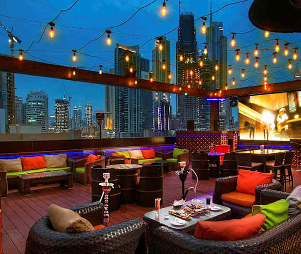 En takterrasse med sittegrupper, dekorative lamper og utsikt over en bysilhuett om kvelden. (AI-generert tekst)