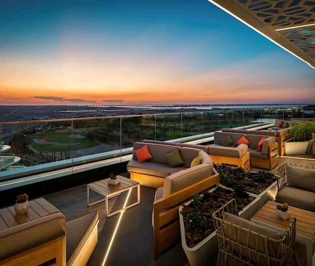 En takterrasse med elegante sittemøbler og glassrekkverk som gir panoramautsikt over landskapet i solnedgang. (AI-generert tekst)