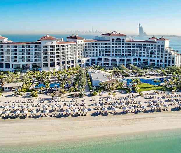 Et stort feriested med bassenger, solsenger og en hvit sandstrand ved havet. (AI-generert tekst)