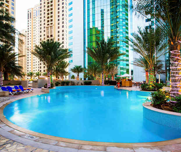 Et utendørs svømmebasseng omgitt av palmer med høyhus i bakgrunnen. (AI-generert tekst)