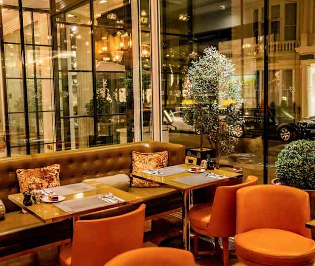 En restaurant med oransje stoler og glassvegger som vender ut mot gaten. (AI-generert tekst)