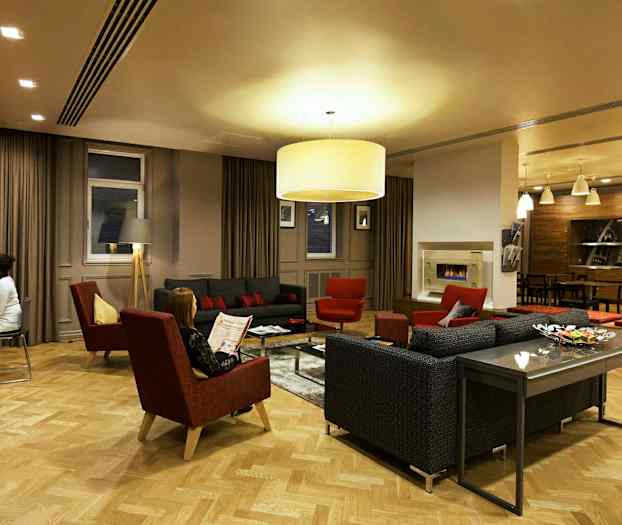 Et elegant oppholdsrom med sofaer, lenestoler og et sofabord omgitt av varm belysning og moderne innredning. (AI-generert tekst)