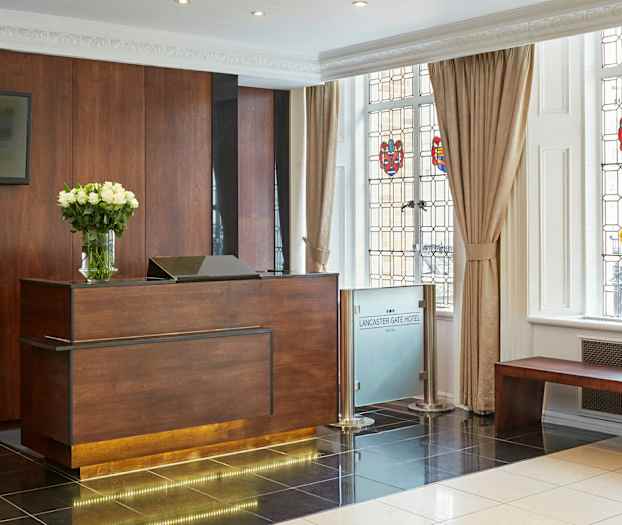 Hotellresepsjon med et skrivbord i tre og en vase med hvite blomster, ved siden av vinduer med fargede dekorasjoner. (AI-generert tekst)