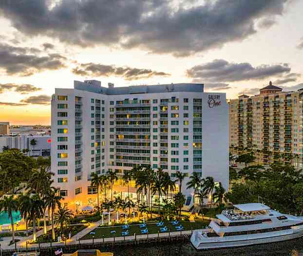 En boligblokk med balkonger, svømmebasseng og en båt er synlige i forgrunnen. Solnedgangen skaper en varm bakgrunn. (AI-generert tekst)