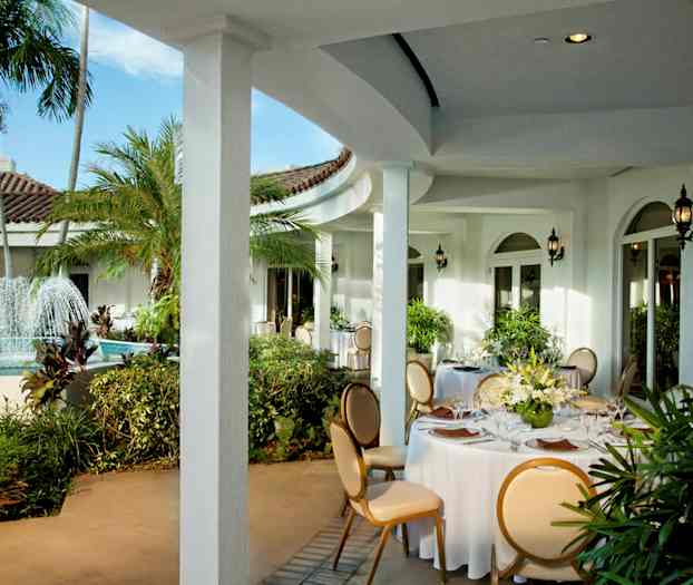 En utendørs terrasse med en fontene og runde bord dekorert med hvite duker og blomsteroppsatser. (AI-generert tekst)