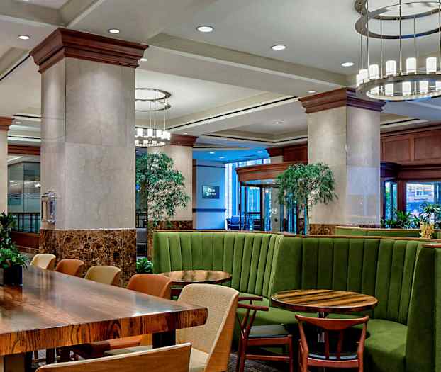 Et moderne innredet interiør med grønne bås-sitteplasser og trebord, omgitt av planter og belysning. (AI-generert tekst)