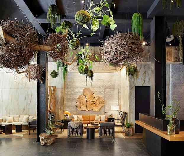 En interiør med naturlige dekorasjoner, som grener og planter hengende fra taket. Det er sitteplasser og bord med dekorasjoner i midten. (AI-generert tekst)