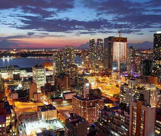 Et nattlig bymiljø med flere opplyste bygninger og gater, med en elv i bakgrunnen. (AI-generert tekst)