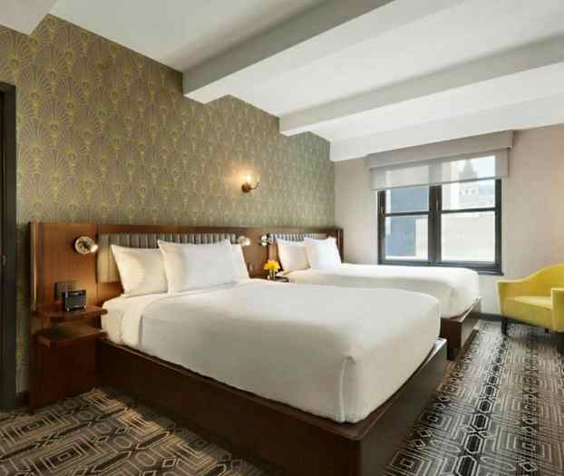 Et hotellrom med to store senger, en gul lenestol, dekorative tapeter og et vindu. (AI-generert tekst)