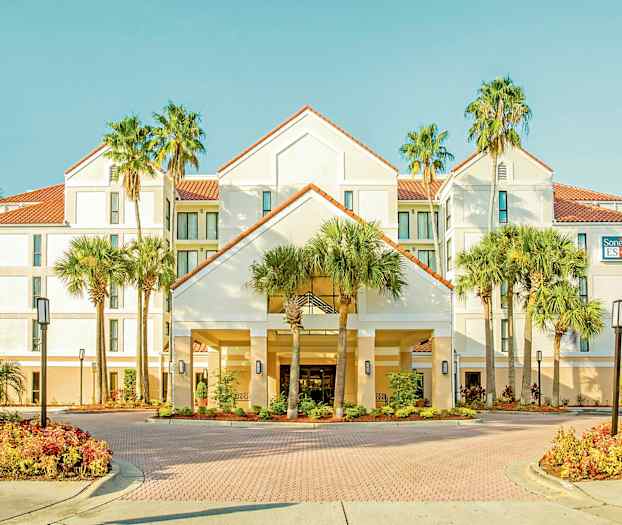 Bilde av et hotell med hvit fasade, røde takstein, omgitt av palmer og velstelte hager. (AI-generert tekst)