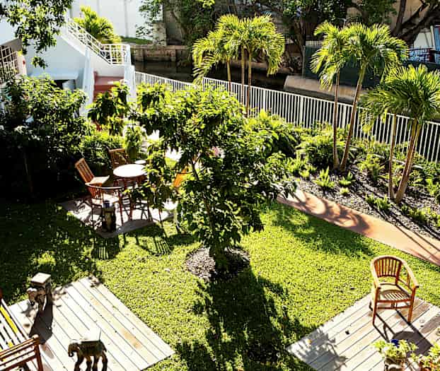 Utsikt over en grønn hage med flere trær og blomsterbed. Det er utemøbler på treplattformer plassert på plenen. (AI-generert tekst)