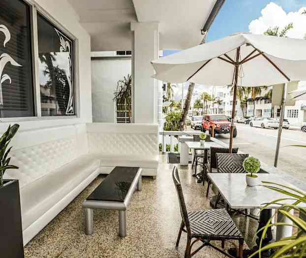 En uteservering med hvite møbler og parasoller i et bymiljø. (AI-generert tekst)