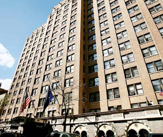 En høy bygning med brun fasade og mange vinduer, med flagg og innganger nederst. (AI-generert tekst)