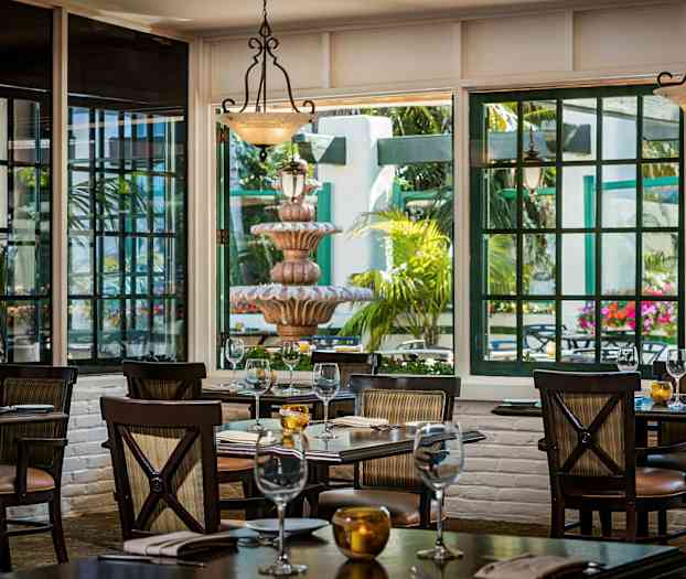 Bilde av en restaurant med oppdekkede bord, store vinduer som slipper inn lys og viser en uteplass med en fontene og grønne planter. (AI-generert tekst)